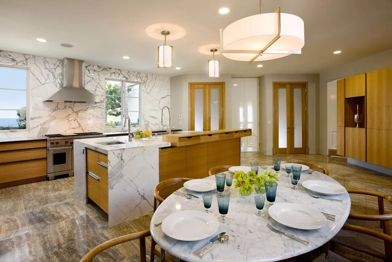 Kitchen features white marble countertops, wood cabinets, stainless steel stove and hood, and adjacent marble dining table with wooden chairs.