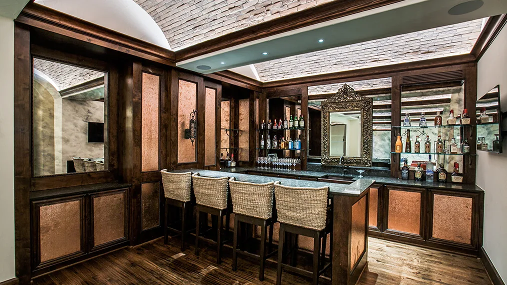Home bar with vaulted brick ceiling, dark wood paneling, and decorative mirror behind the counter.