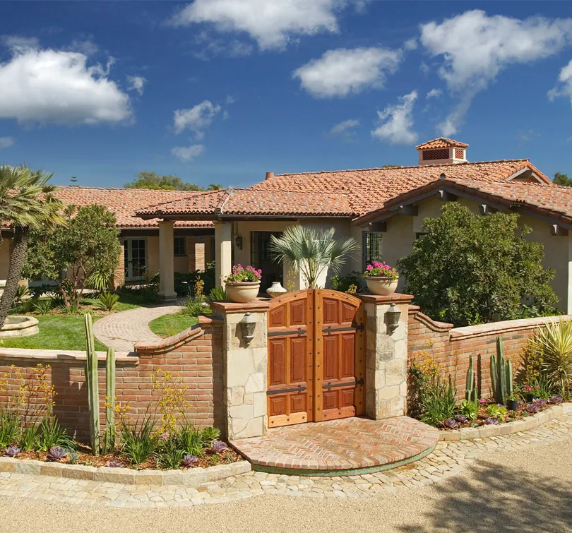 Montecito Andalusian Estate features a terracotta tile roof and a wooden front gate set in a brick and stone perimeter wall.