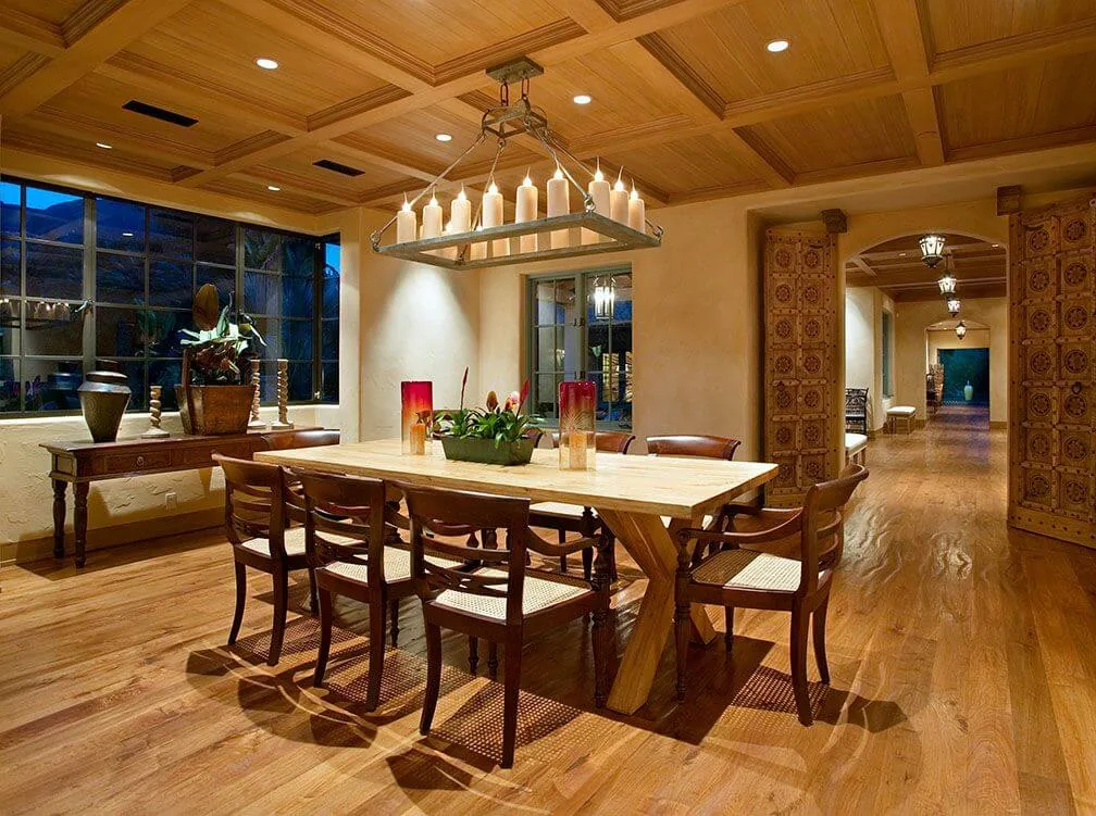 Dining room featuring wood-paneled ceiling, hardwood floors, and wrought iron candle chandelier in a home with carved wooden doors and archways.