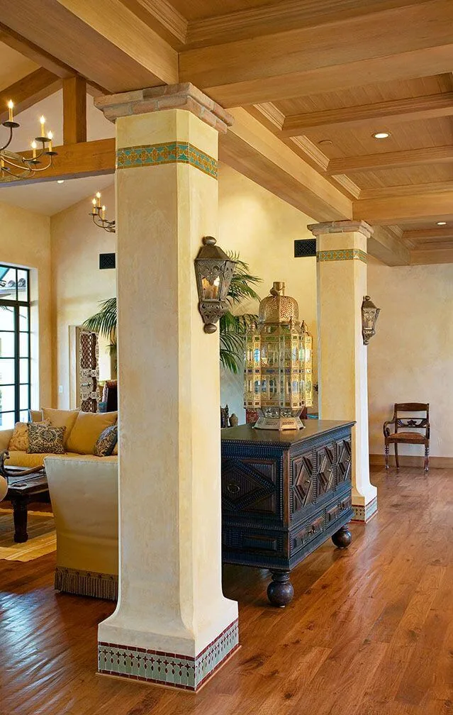Living room interior features plaster columns with decorative tile bases and wooden coffered ceiling with chandeliers.