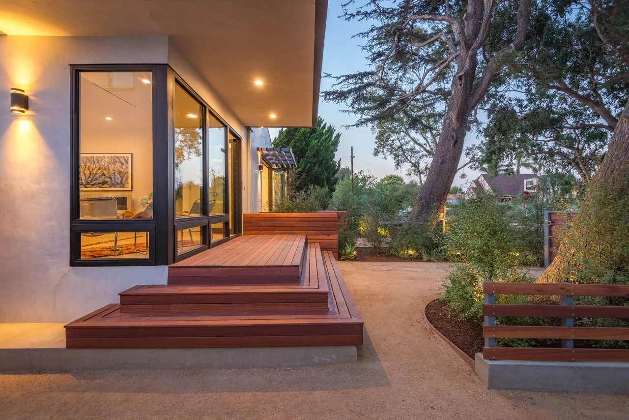This modern bungalow exterior features a wooden deck with built-in bench seating and large corner windows with black frames.
