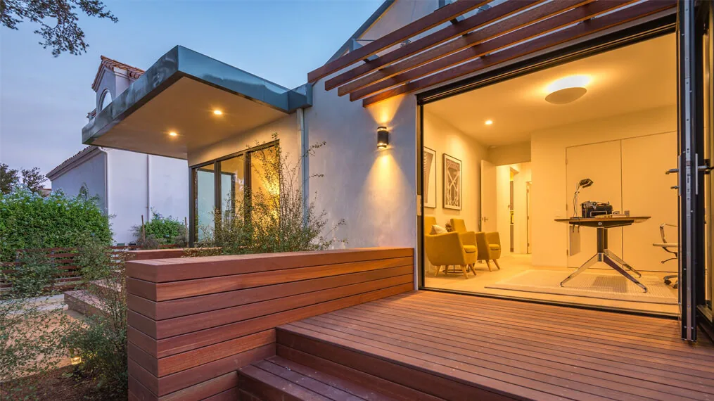Modern bungalow exterior deck and interior office space illuminated by dusk lighting.