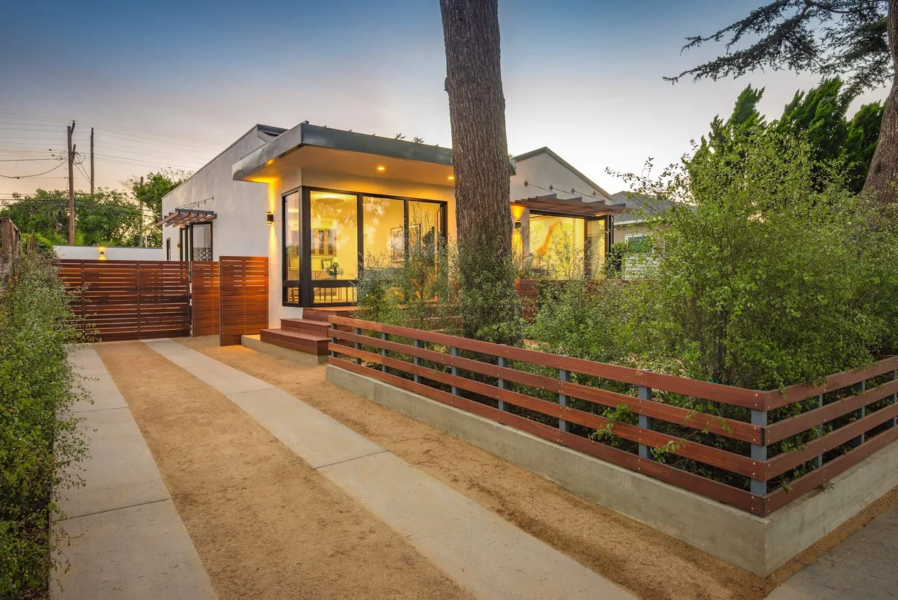 Modern bungalow exterior with flat roof, black window frames, and wood fencing along the driveway and yard.