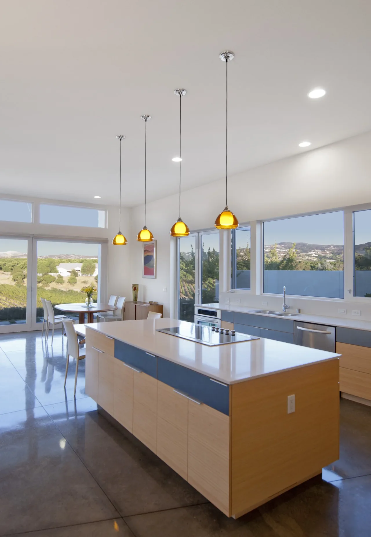 Kitchen with a large island, yellow pendant lights, and expansive windows overlooking a hillside landscape.