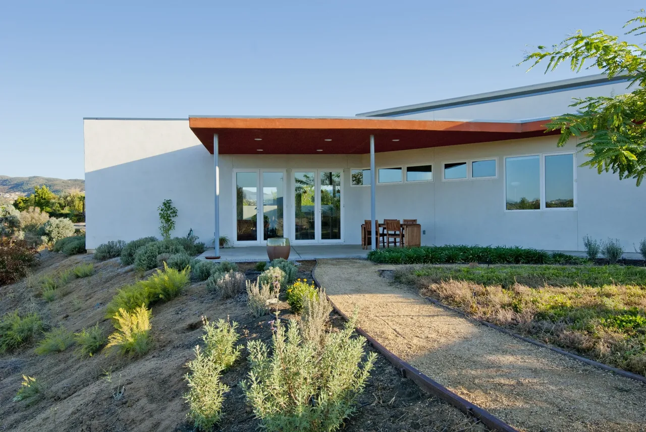 Modern white stucco house with flat roof and covered patio overlooking desert landscaping in a hillside site.