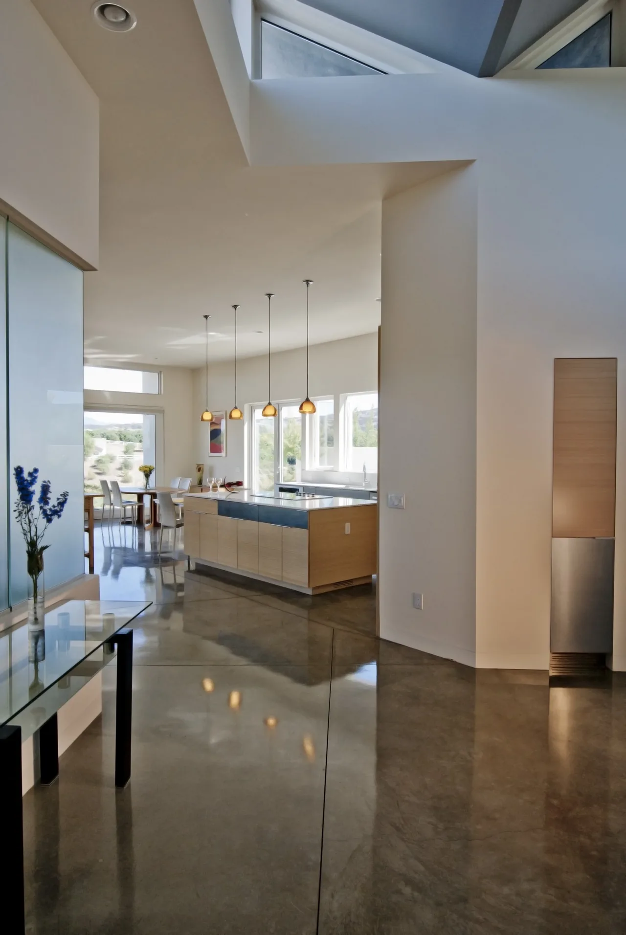 Modern kitchen and dining area featuring a large kitchen island, polished concrete floor, and yellow glass pendant lights.