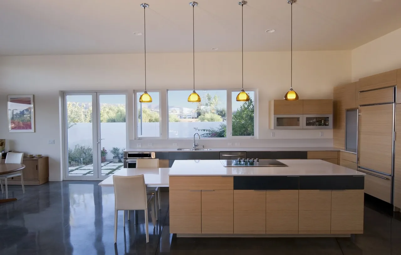 Calle Anita kitchen by MAKE Architecture features wood cabinetry, yellow glass pendant lights, and a polished concrete floor.