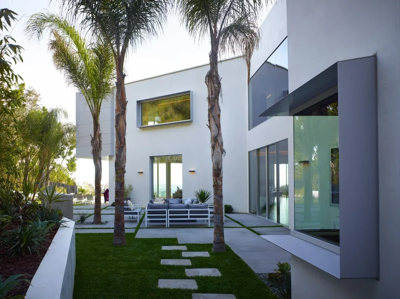 Exterior view of Rising Glen house featuring white stucco walls, large windows, and an outdoor seating area with palm trees.