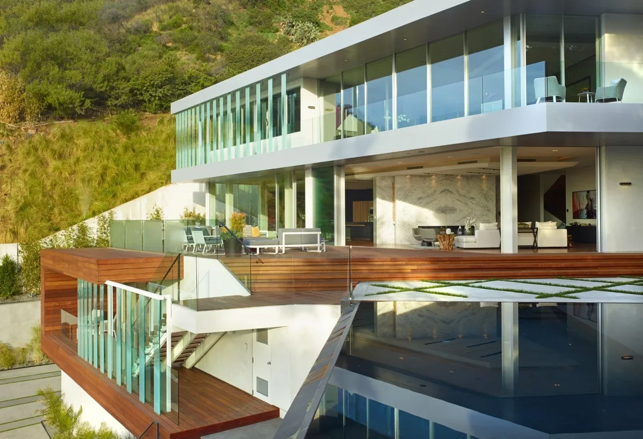 Rising Glen house designed with floor-to-ceiling glazing, glass balcony railing, and an outdoor pool on a hillside setting.