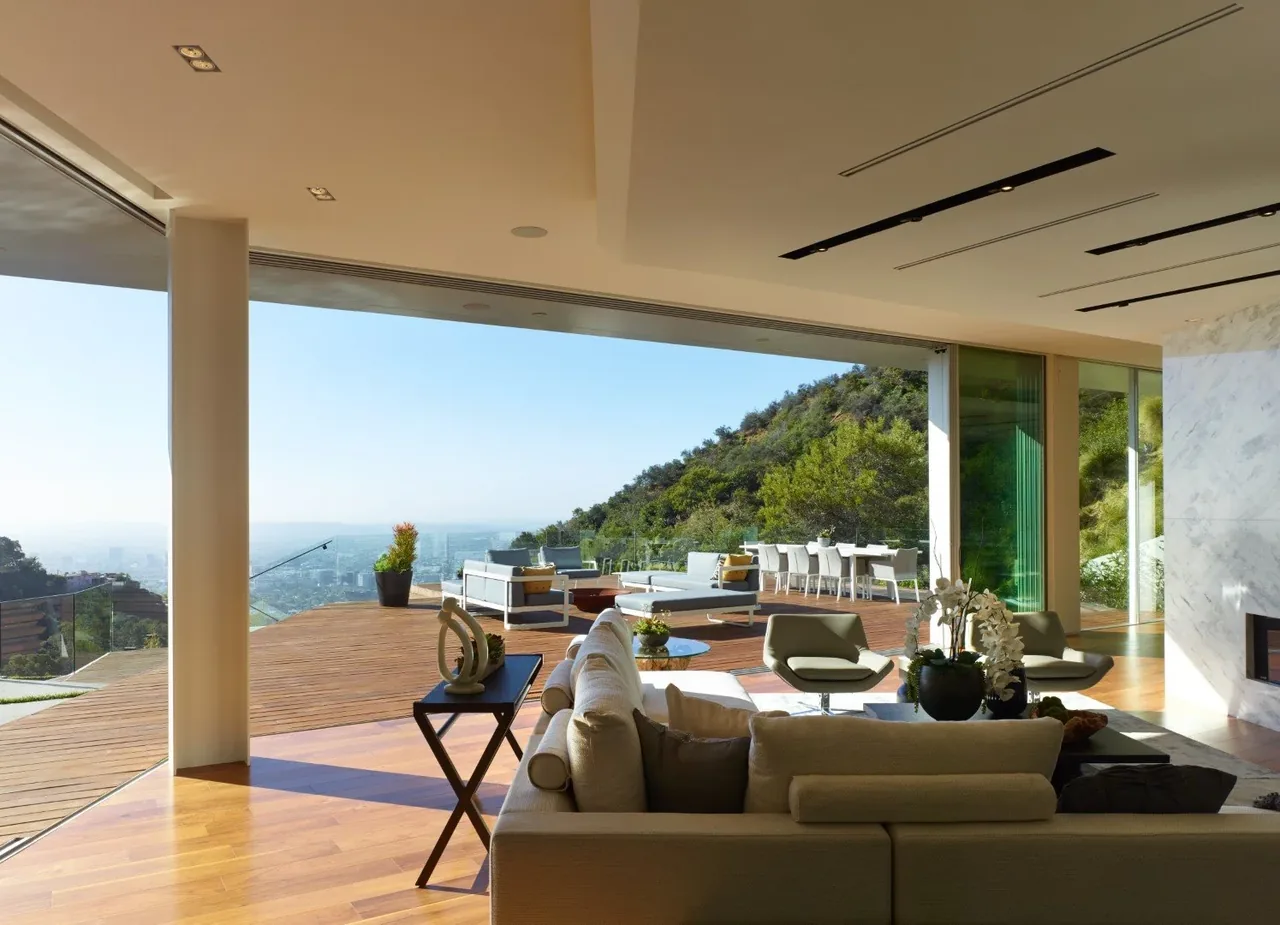 Living room with sliding glass doors opens to a wood deck overlooking a hillside and cityscape.