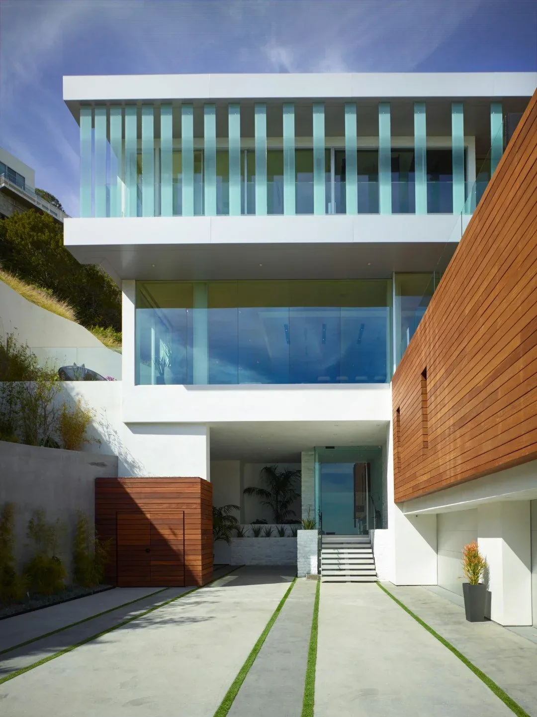 Rising Glen project features a white modern home with vertical glass fins and wood siding on a hillside.