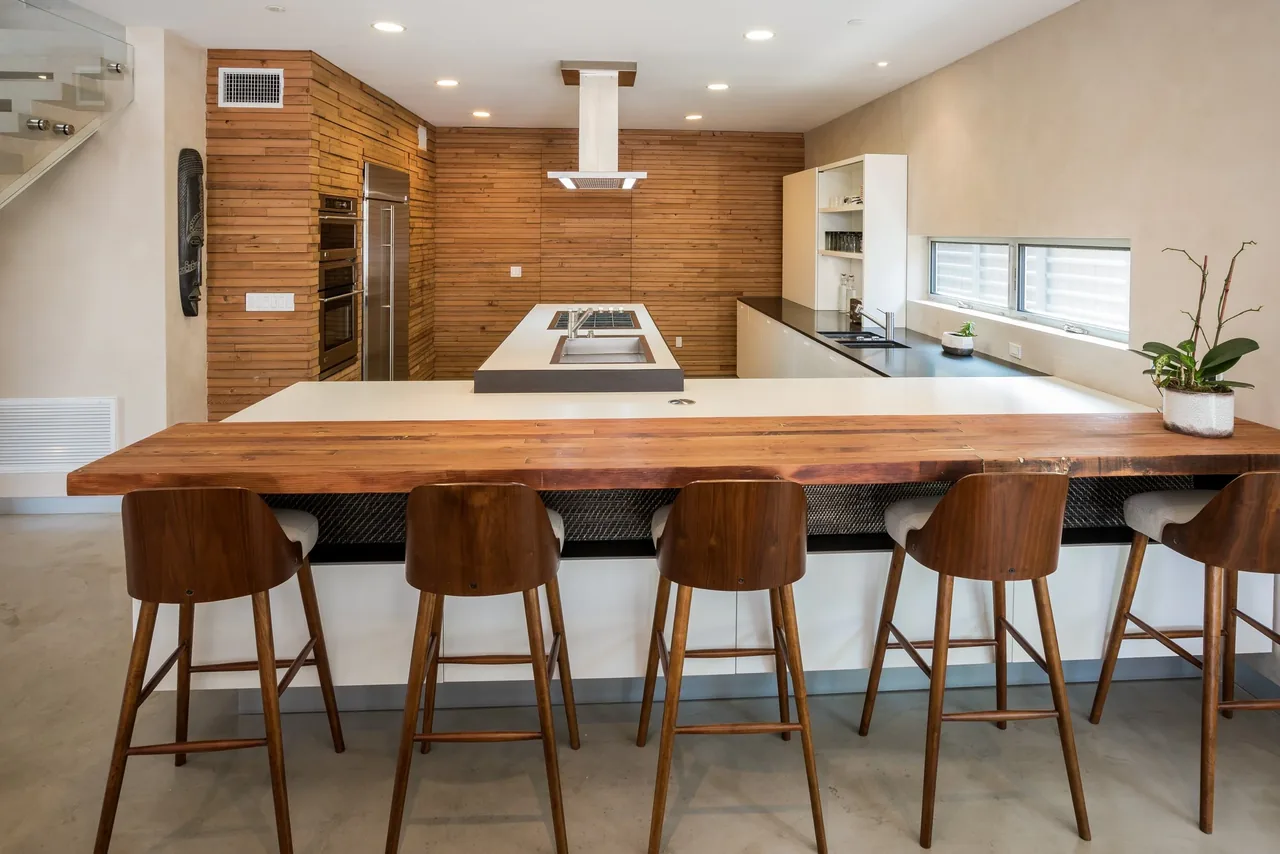 Kitchen featuring a wooden panel accent wall, island with cooktop and hood, and a wooden counter with stools.