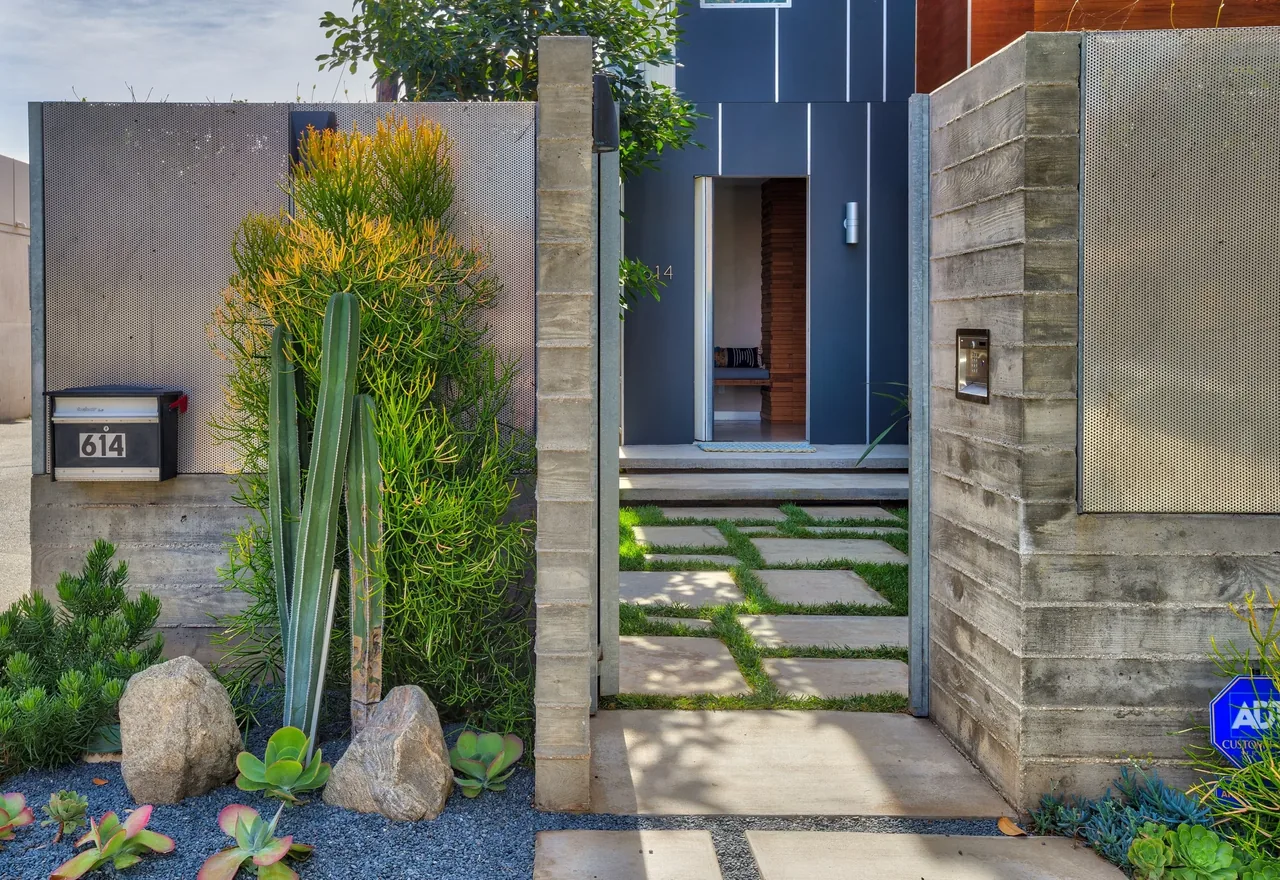 Concrete stepping-stone path with grass leads through a concrete and metal entrance to the front door of a modern home.