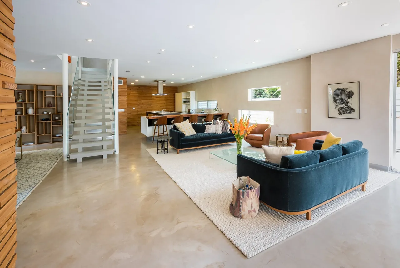 Open living and kitchen area with polished concrete flooring and a glass staircase in a modern California home