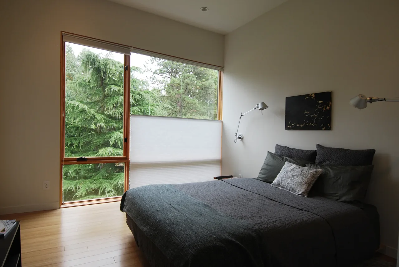 Bedroom in Greenwood House featuring large wood-framed windows and dark gray bedding.