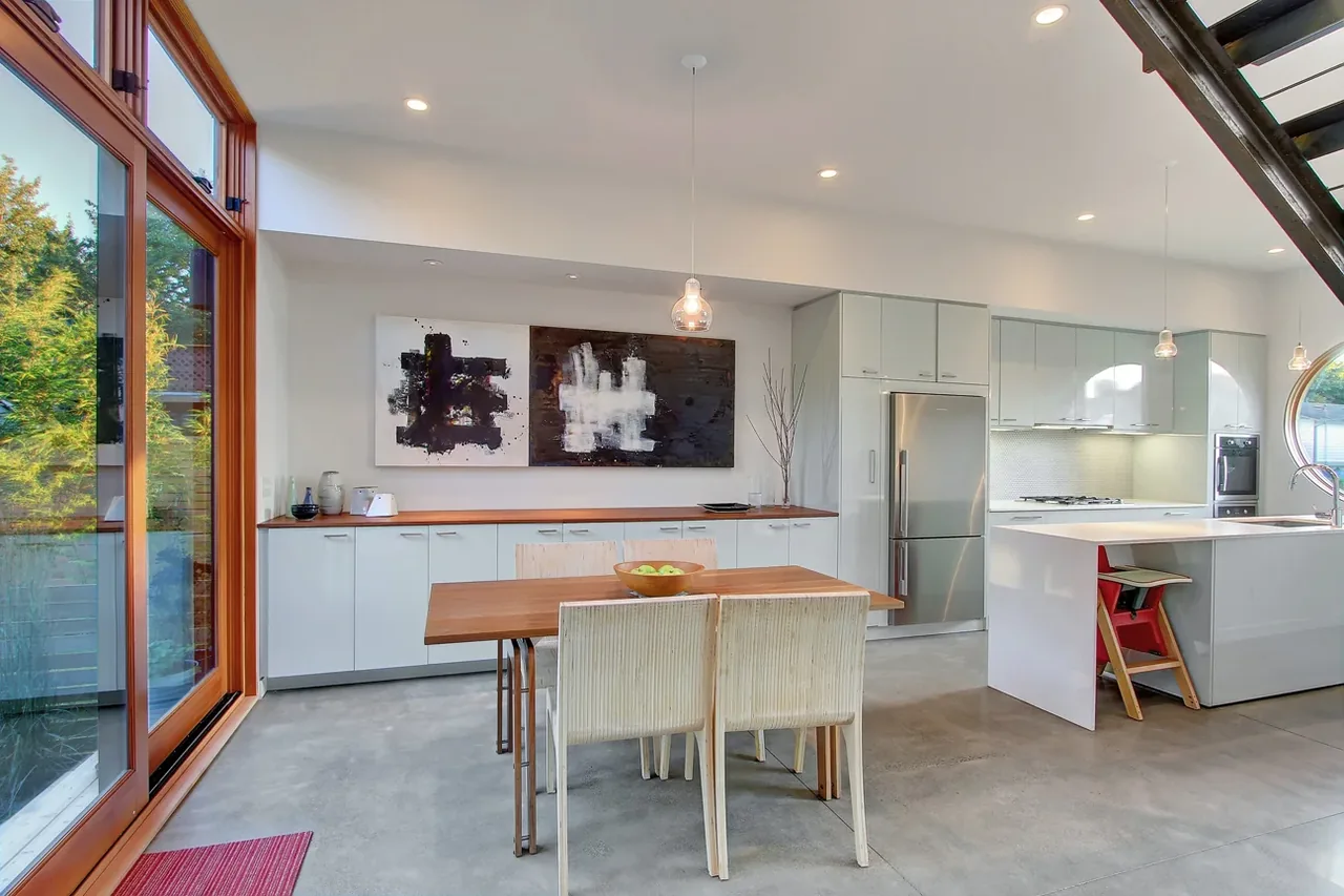 Kitchen and dining space in Greenwood House features white cabinetry, wood accents, and a large sliding glass door.