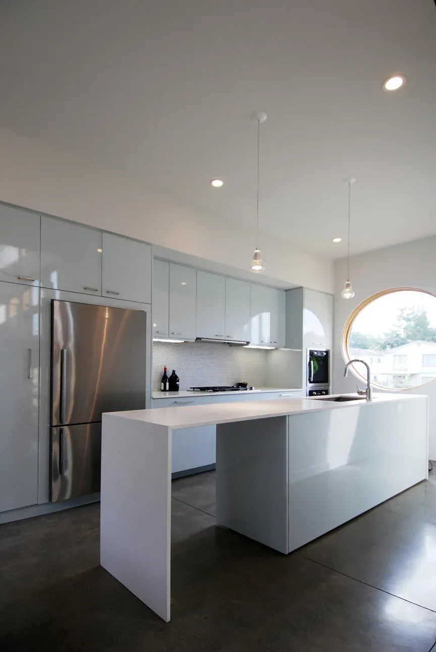 The Greenwood House kitchen features a sleek white island, stainless steel appliances, and a distinctive round window.