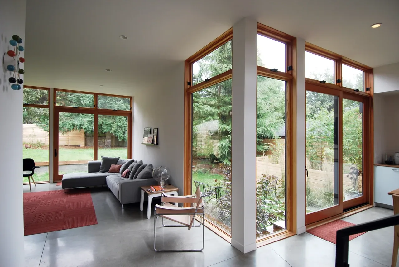 Living room with floor-to-ceiling wood-framed sliding glass doors and large windows opening to a landscaped backyard with wooden fence.