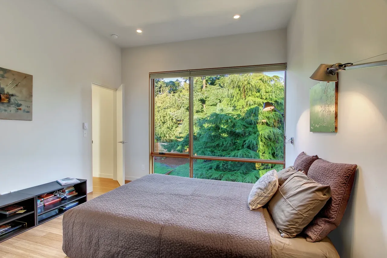 This bedroom features a large window providing a view of lush greenery outside.
