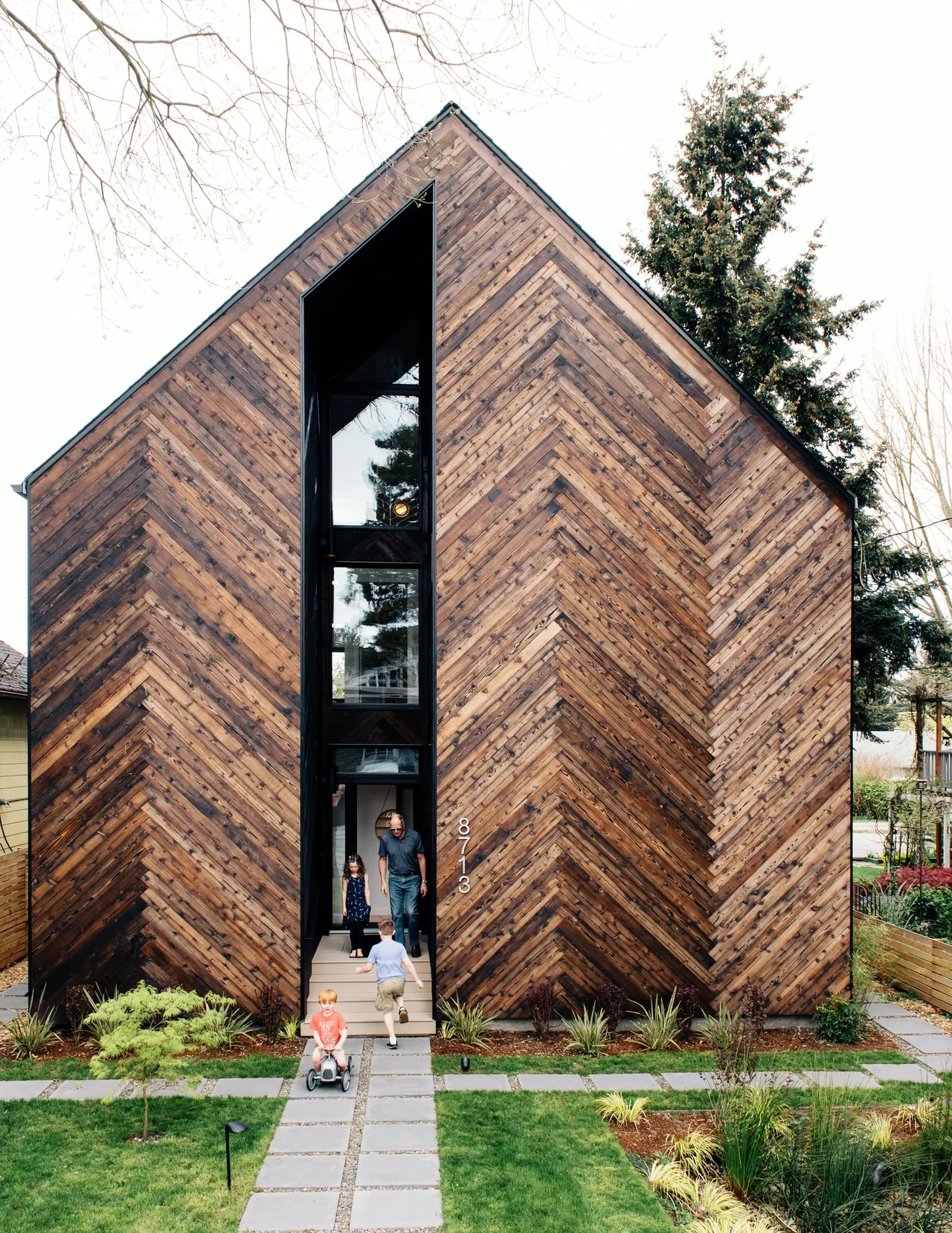 Modern house exterior featuring chevron-patterned wood siding and a tall vertical window in the entry area.