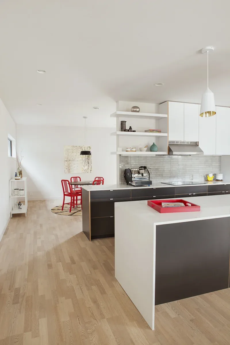 A modern kitchen features black and white cabinetry with a minimalist dining area that has red chairs.