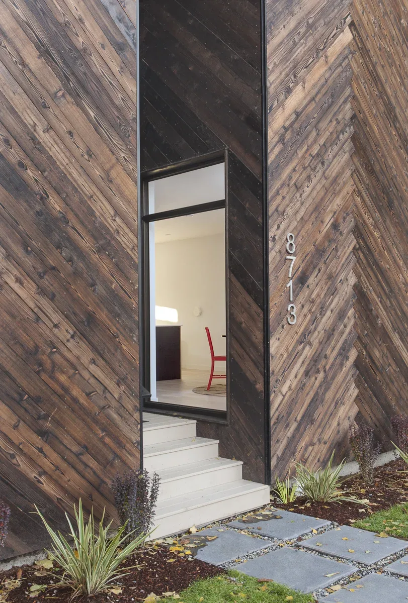 The Palatine Passive House features a wood siding facade with a narrow glass entry door and white stairs.