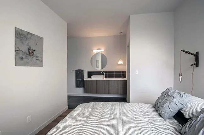 A bedroom opens to a bathroom featuring a dark floating vanity and round mirror.