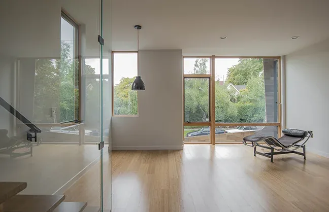 Living room with floor-to-ceiling wood-framed windows and a black lounge chair on wood flooring.