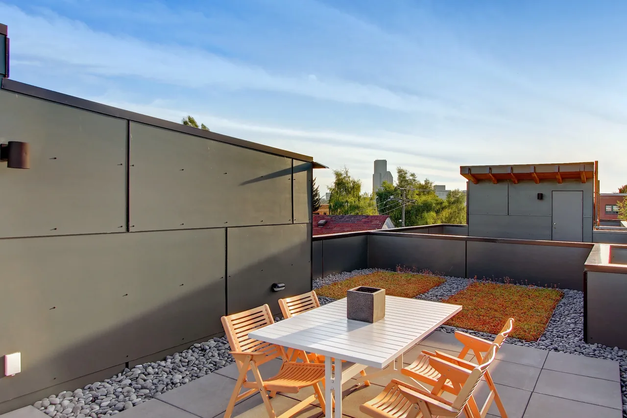 Rooftop outdoor living space featuring black metal panel walls, garden beds, and light wood furniture at 18th Ave project.