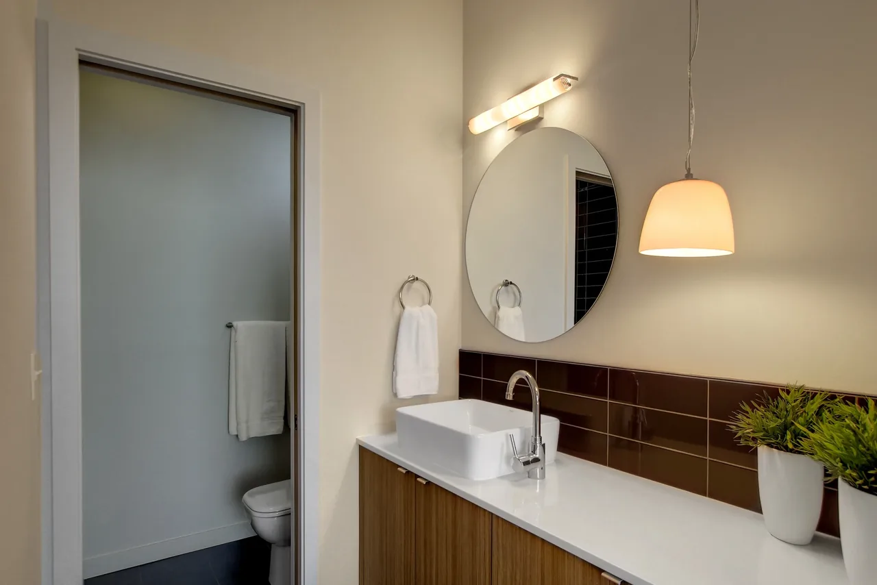 Modern bathroom featuring a rectangular vessel sink on a wooden vanity with a round mirror, pendant light, and brown tiled backsplash.