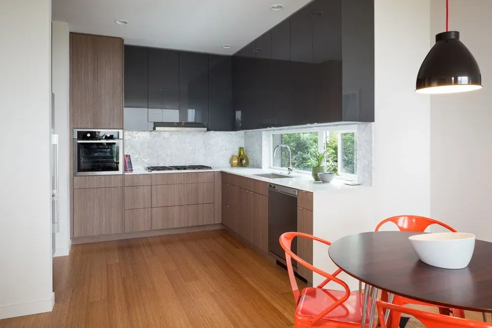 Kitchen area featuring wood cabinetry, white countertops, and a round dining table with orange metal chairs.
