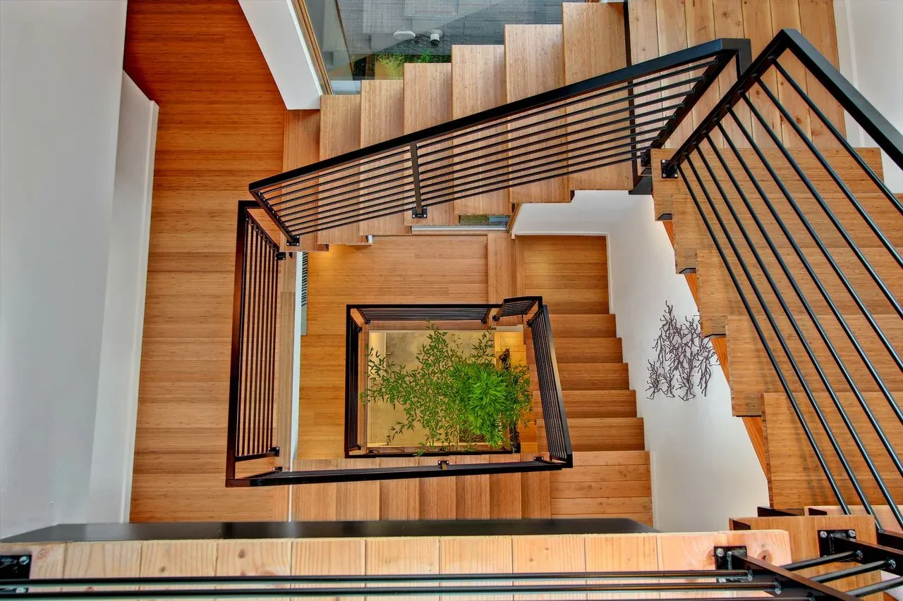 Stairwell featuring wood stairs with black metal railings enclosing a central plant.