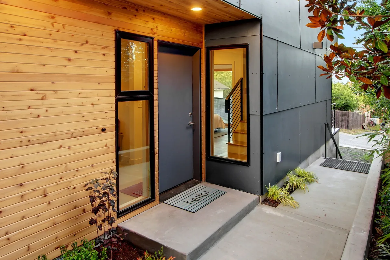 Front entry of the 18th Ave project with natural wood siding and dark metal panel facade by Malboeuf Bowie Architecture.
