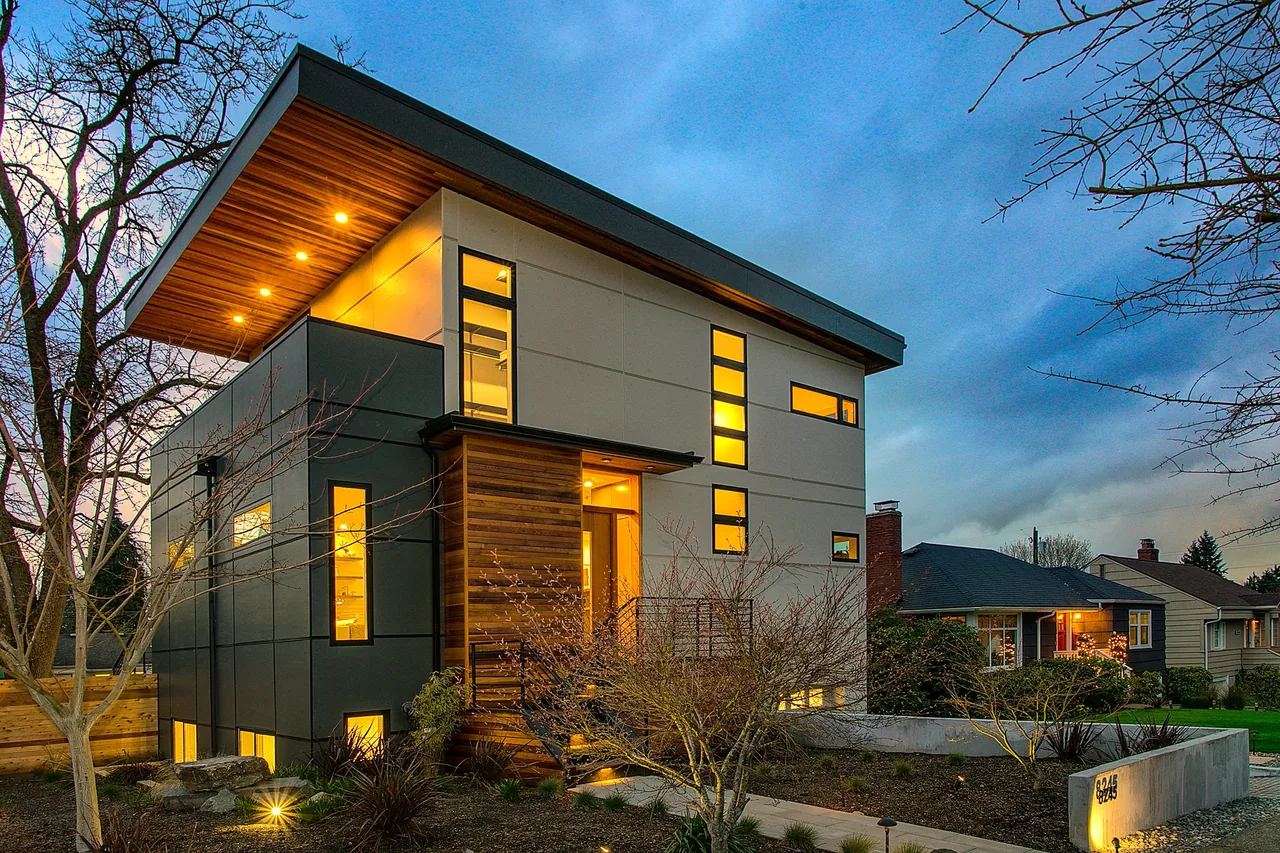 The Wedgwood features a modern exterior with black window frames and mixed wood and panel siding, illuminated at dusk in Seattle.