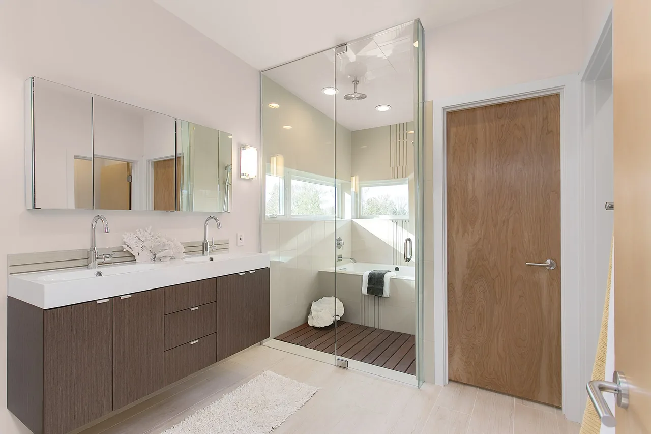 Bathroom featuring a double sink vanity, large mirrors, and a glass shower enclosure with a built-in tub.