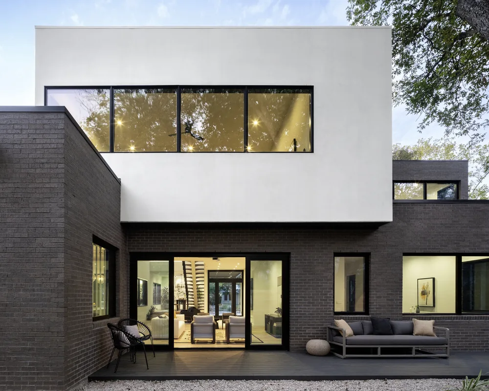 Contemporary Bull Creek residence features dark brick and white stucco facade with floor-to-ceiling black framed windows and outdoor seating patio.