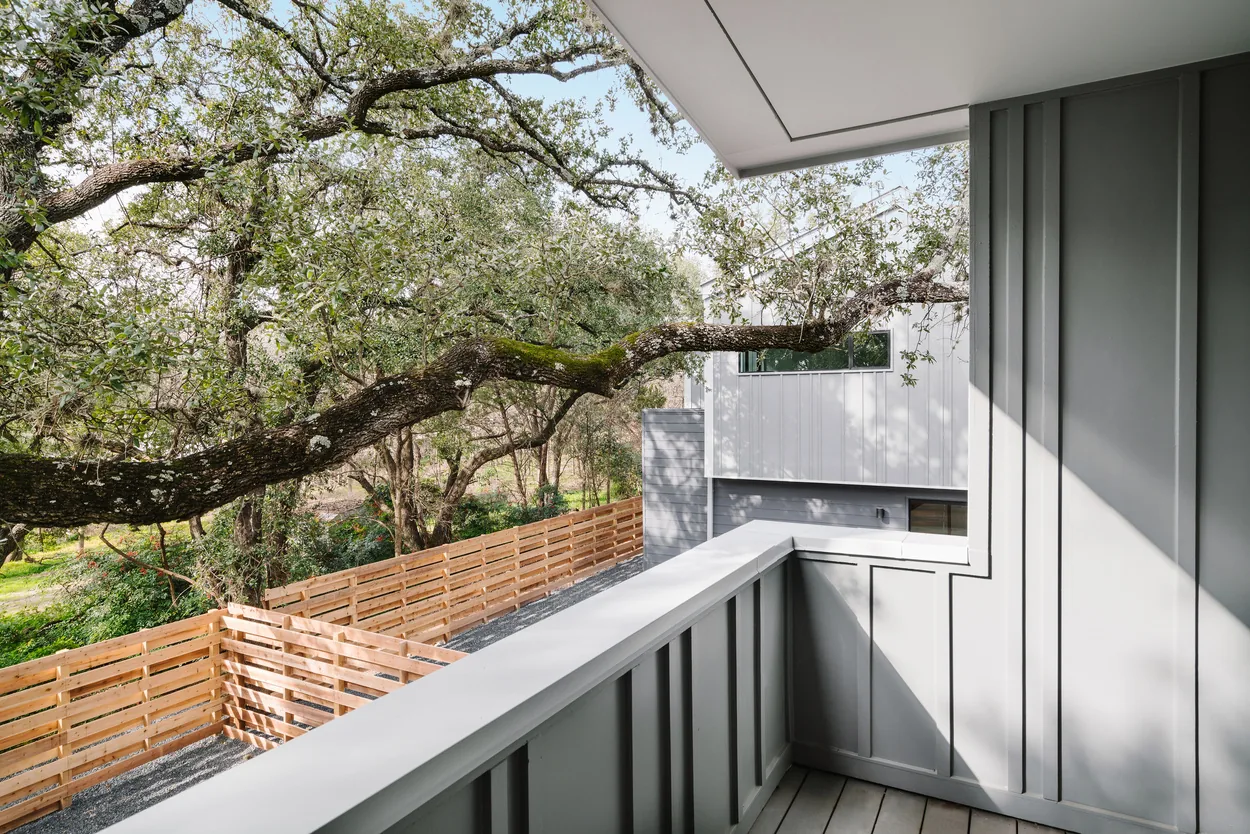 Gray paneled balcony with view of wood fence and neighboring white and gray siding in a duplex setting.