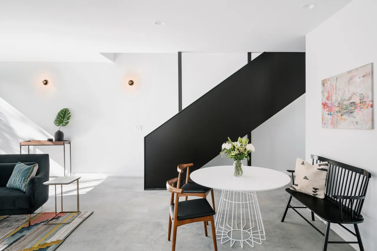 Dining space features a round white table, wooden and black chairs, and a black stair with white walls.