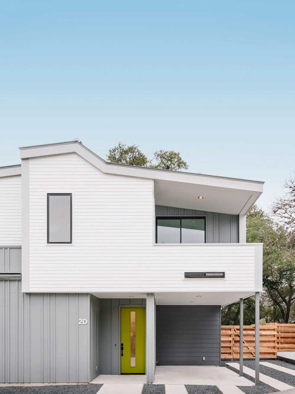Exterior front view of Clawson Duplexes featuring modern design with gray board and batten siding, white horizontal siding, and a green front door.