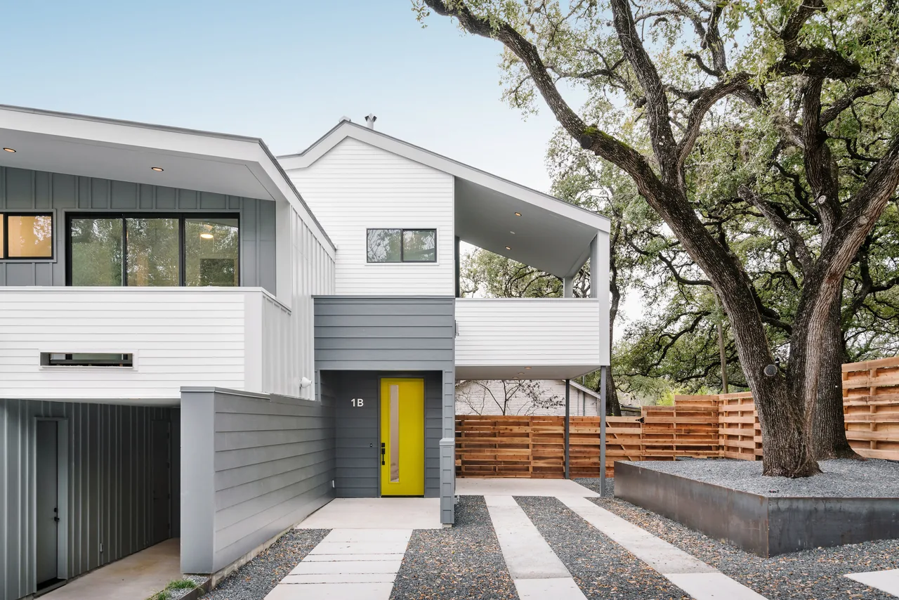 The Clawson Duplexes feature contrasting white and gray siding with sloped roofs and a yellow entry door.