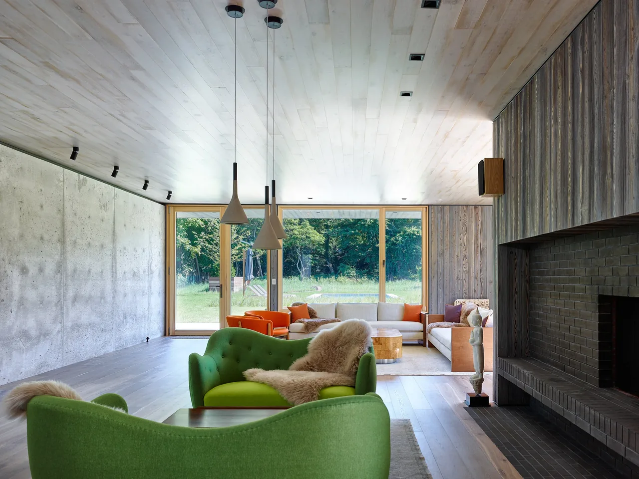 Living room with large glass sliding doors overlooks greenery, featuring green and orange furniture and wood paneling.