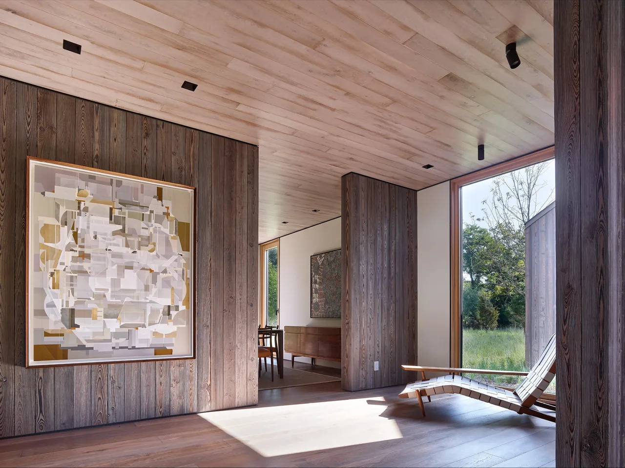 Interior view of a modern room featuring dark vertical wood siding walls and a large fixed window overlooking greenery.