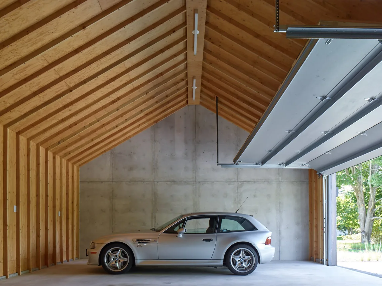 Garage interior featuring exposed wood beams and concrete walls with an open overhead door.