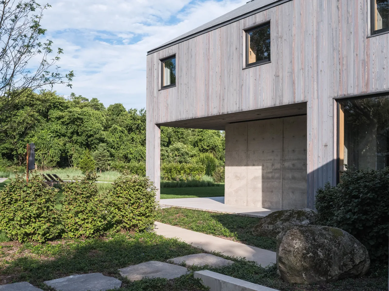 House in the lanes 4tkaf features vertical wood siding and a concrete accent wall with large windows overlooking the landscaped yard.