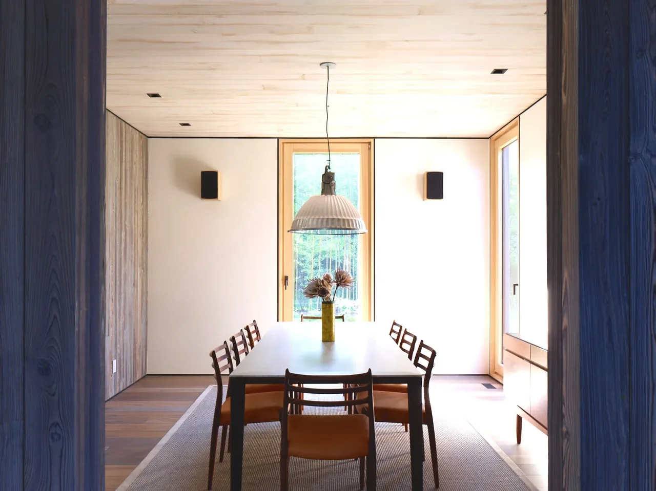 Dining room featuring a rectangular table with six chairs and a large pendant light, framed by natural wood window trim.