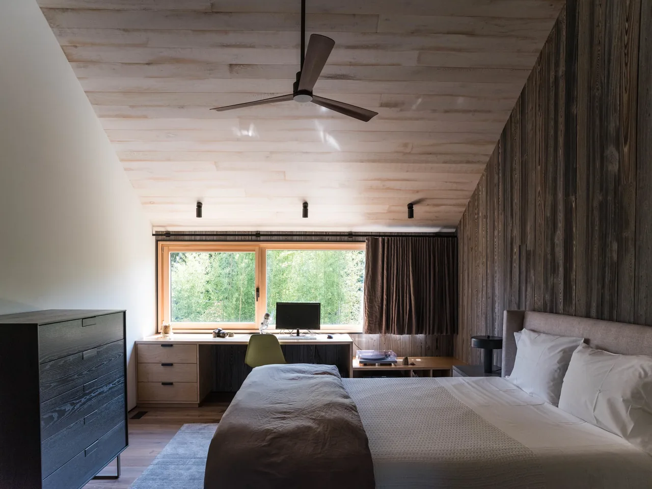 Bedroom featuring a wood accent wall and a wide window with a wooden frame overlooking greenery.