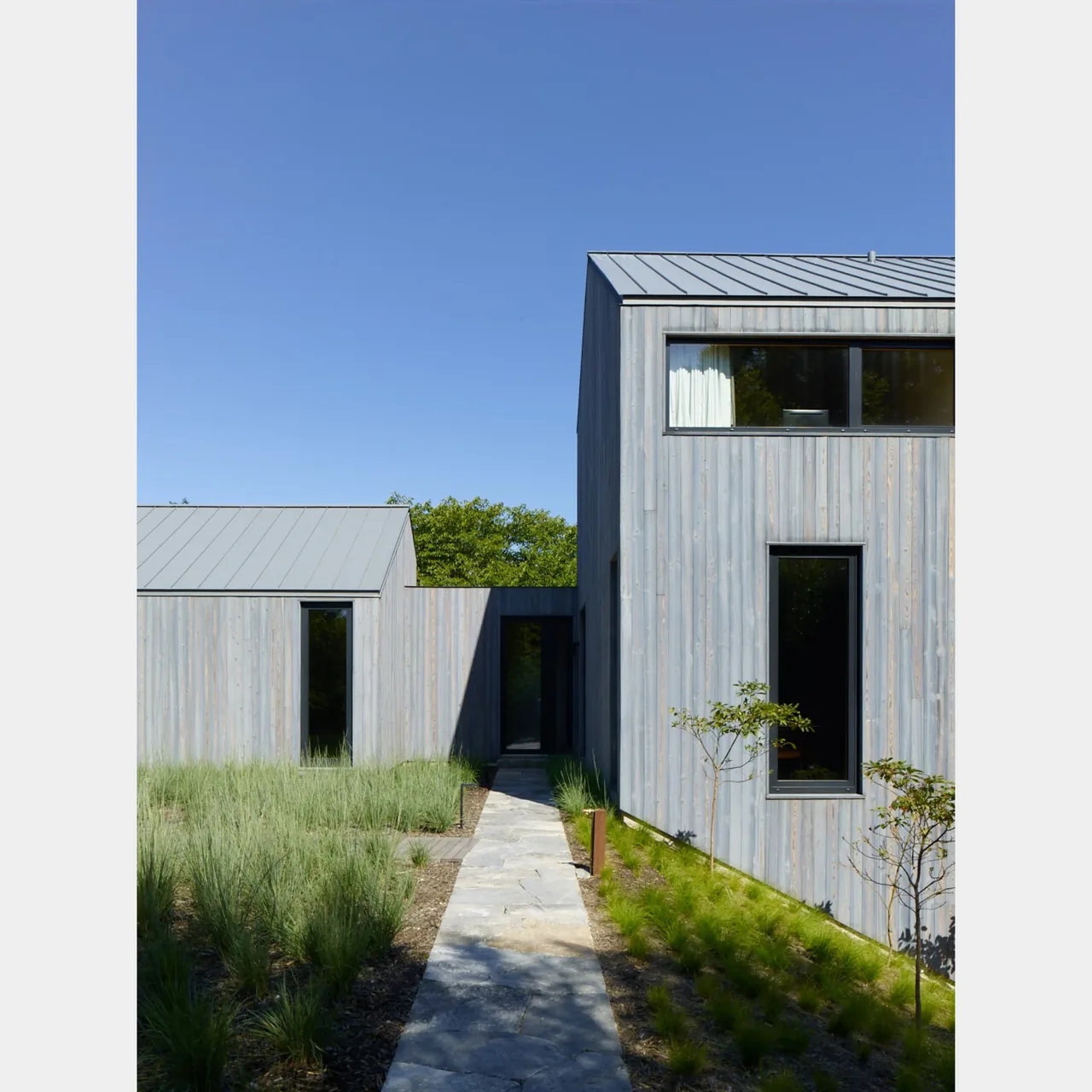 The house in the lanes 4tkaf features vertical wood siding and standing seam metal roofs with narrow black-framed windows.