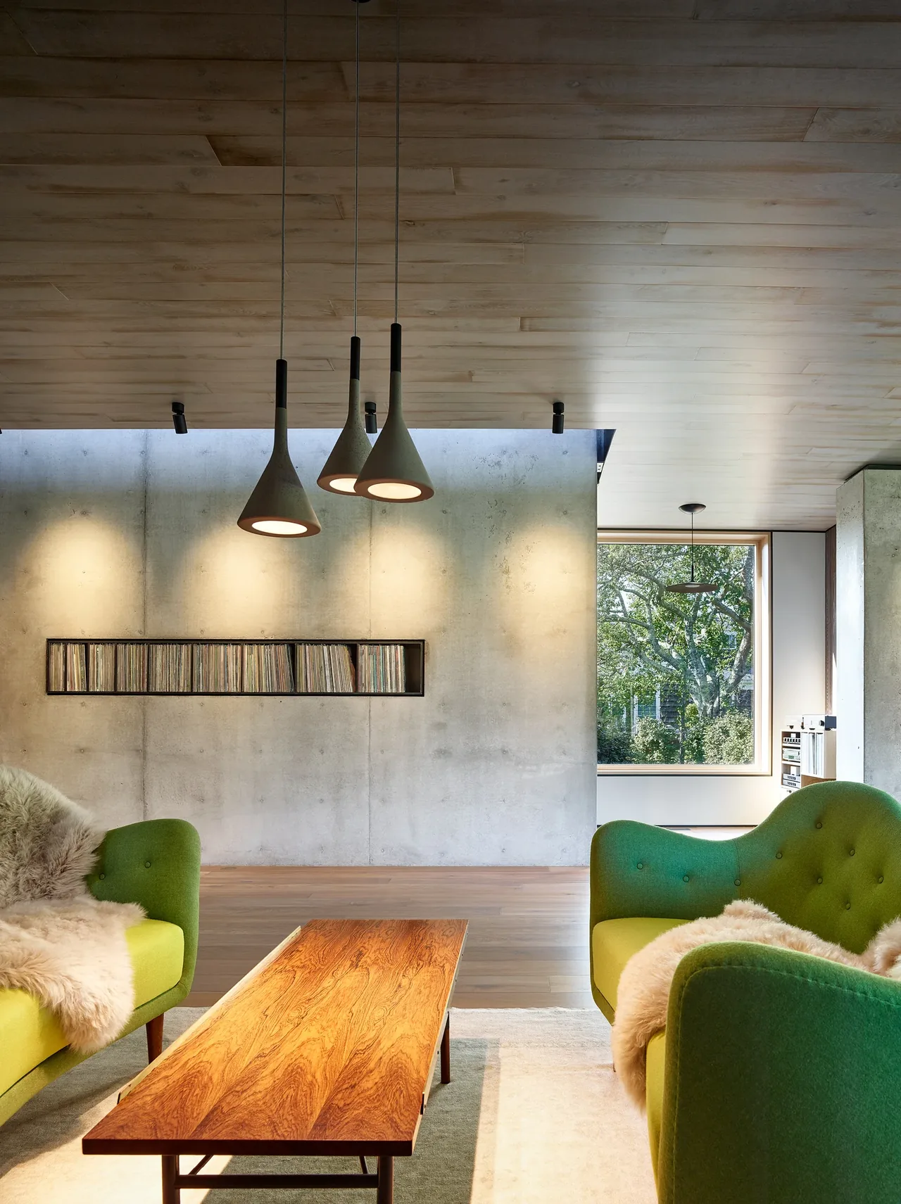 Living space with concrete accent wall, mid-century style green chairs, and natural light from a large window.