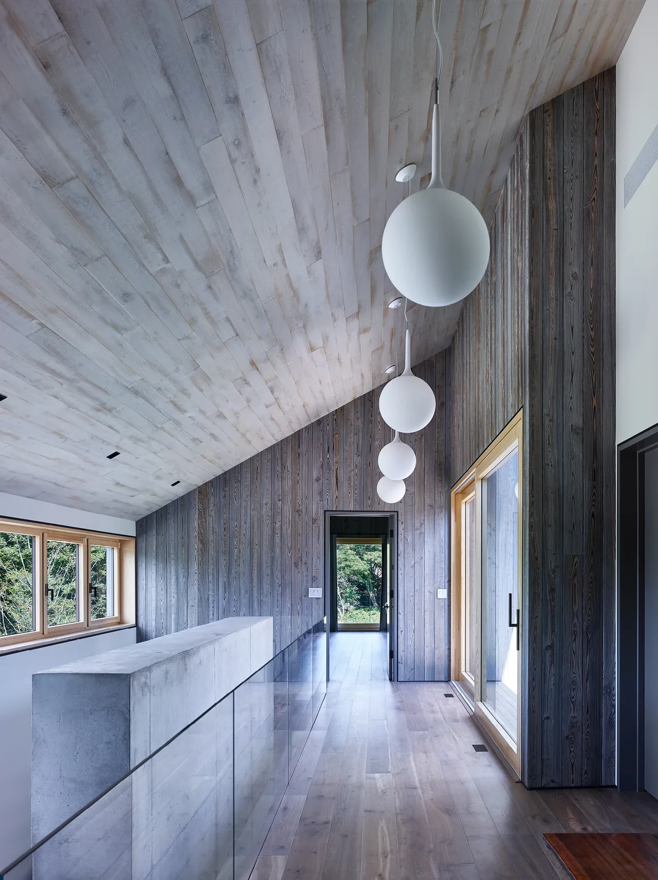 Hallway with wood plank ceiling and wall, large windows with wood frames, and globe pendant lights.